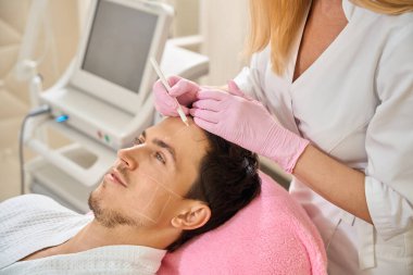 Uzman, hastaların yüzüne işaret koyar. Kadın da özel kalem kullanır.