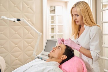 Kozmetik uzmanı hastaların yüzüne iz bırakır. Bir kadın özel bir kalem kullanır.