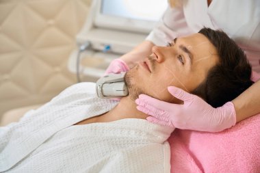 Uzman, çene bölgesindeki bir müşteriye mikronedle RF uyguluyor. Adam kozmetik kürsüsünde oturuyor.