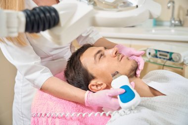 Ultrasonik yüz temizleme ameliyatı geçiren yakışıklı bir adam. Koruyucu eldivenler konusunda uzman.