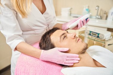 Etkili ultrasonik yüz temizleme ameliyatı geçiren bir adam, alın bölgesi üzerinde çalışan bir uzman.
