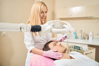 Adam etkili bir yüz temizleme işleminden geçiyor. Alnında bir uzman çalışıyor.