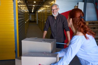 Depoda kutuları olan gülen adam, kutuları boşaltmaya yardım eden kadın.