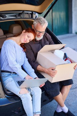 İnsanlar açık bagajın kenarına oturdu, kadın kafasını kocasının omzuna koydu.