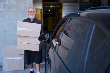 Adam arabadan kutular taşıyor, bir depoda.