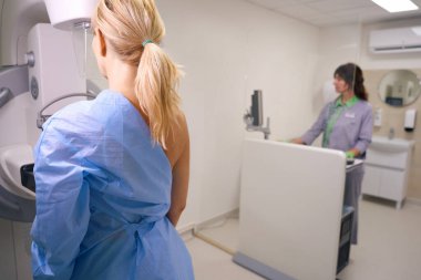 Hasta arka plandaki kontrol konsolu aracılığıyla profesyonel radyolojik teknoloji uzmanı tarafından işletilen mammografi makinesinin önünde duruyor.