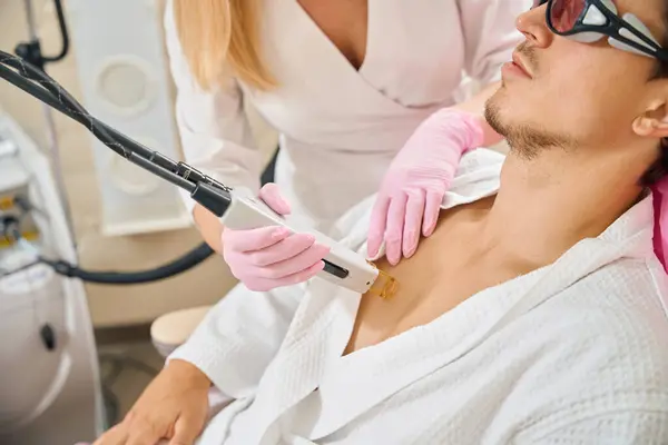 Man undergoes laser hair removal of the chest in a beauty salon, a specialist works in protective gloves