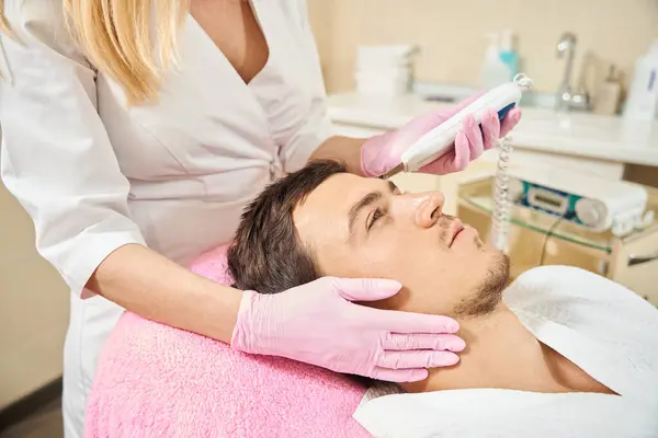 Etkili ultrasonik yüz temizleme ameliyatı geçiren bir adam, alın bölgesi üzerinde çalışan bir uzman.