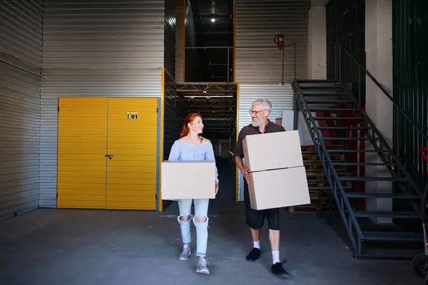 Happy middle-aged couple is in a storage warehouse, people have cardboard boxes with things