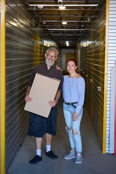 Man with a box and a red-haired lady are in a storage warehouse, people in casual clothes