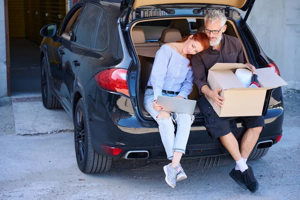 Karı koca açık bagajın kenarında otururken kadın başını kocasının omzuna yasladı.