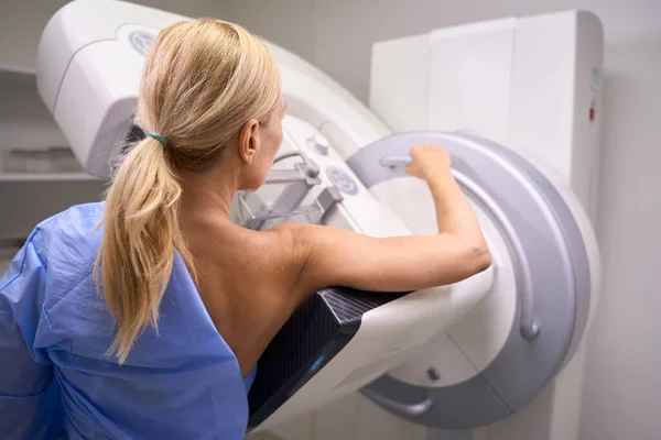 Back view of Caucasian female patient undergoing 3D mammography in radiology room