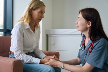 Şefkatli doktor, kliniğin lobisindeki koltukta oturan üzgün kadın hastasını teselli ediyor.