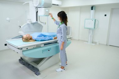 Radyografik sehpanın üzerinde yatmakta olan hastanın röntgen tüpünü yerleştiren teşhis edici radyograf.