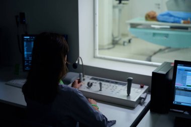 Kontrol odasındaki masada otururken kumanda panelinde hareket eden radyografın arka görünümü