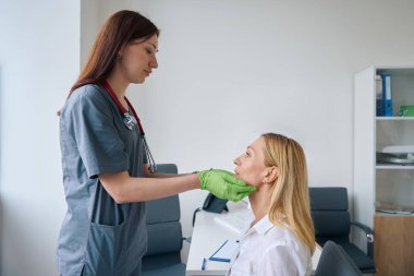 Ciddi bir KBB doktoru. Eldivenleriyle kadın tükürük bezlerini muayene ediyor.