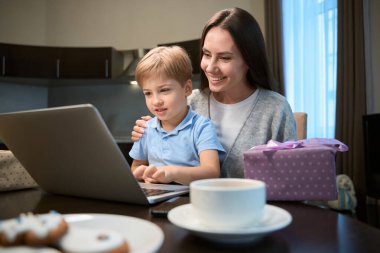 Küçük oğluyla Noel filmi izleyen neşeli bir kadın web mağazasından hediye almaktan zevk alıyor.