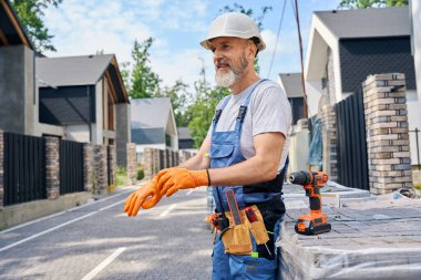 Gülümseyen duvar ustası lastik eldiven giyer ve kaldırım taşlarına yaslanır.