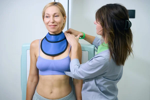 Erwachsene Frau Lehnt Röntgenwand Während Radiologe Schilddrüsenkragen Ihren Hals Wickelt — Stockfoto