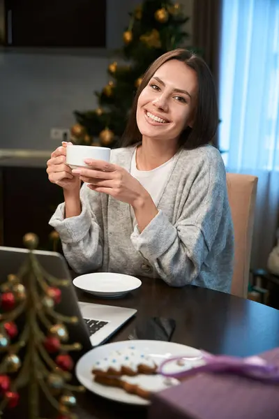 满意的妇女在家中享用新年假期 使用笔记本电脑喝咖啡或茶 — 图库照片
