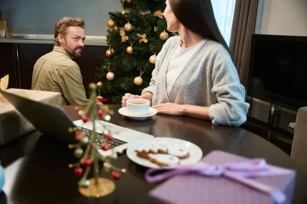 一个英俊的男人装饰着圣诞树 而一个女人则在家里喝茶和过冬 — 图库照片
