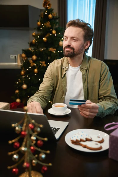 Satisfied man dreaming about presents for his family buying gifts online paying with credit card