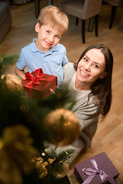 寒假期间 快乐的女人牵着小儿子 手里拿着礼物盒站在圣诞树旁 — 图库照片