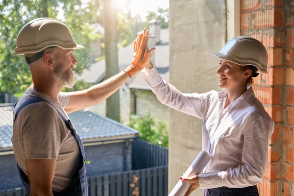 Smiling female construction superintendent giving high-five to contractor inside unfinished residential house
