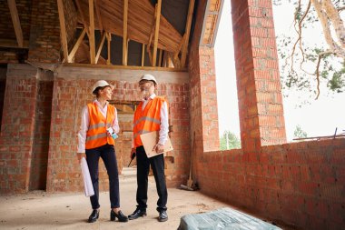 Gülümseyen inşaat müdürü bitmemiş bir konutun odasında dururken ustabaşıyla konuşuyor.