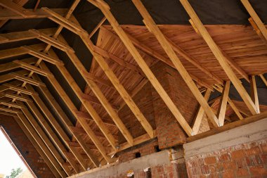 Kırmızı tuğlalı duvarları ve ahşap çatı kirişleri olan tamamlanmamış konut binasının alçak açısı