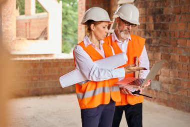 Tamamlanmamış bir binada meslektaşına dizüstü bilgisayarda bir şey gösteren mimar.