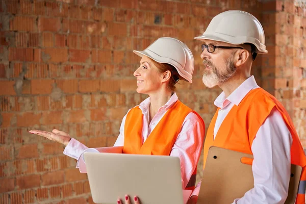 Joyous Female Engineer Pointing Something Colleague While Standing Brick Wall — Stock Photo, Image