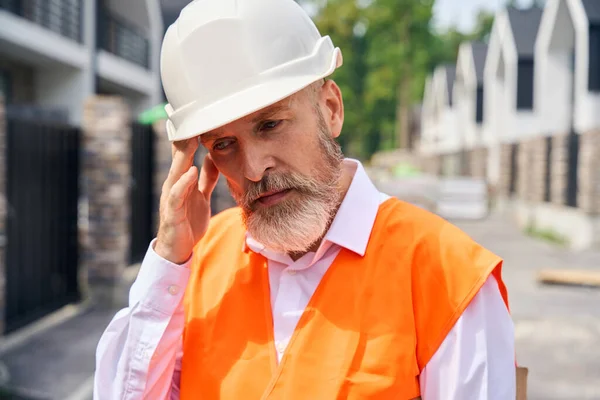 Sokak Evlerinin Arasında Dikilirken Şapkalı Şakağına Dokunan Yorgun Inşaat Müfettişinin — Stok fotoğraf