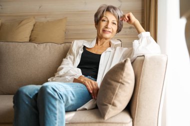 Güzel yaşlı bayan rahat bir kanepede dinleniyor, rahat kıyafetler giyiyor.