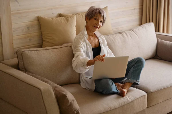 Pretty woman with a short haircut sits with a laptop on a cozy sofa in an eco-design room