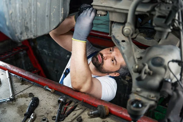 Concentrated car mechanic is tightening nut on motor vehicle underbody using spanner
