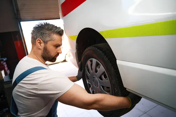 Serious focused automotive service technician installing new wheel on vehicle in garage
