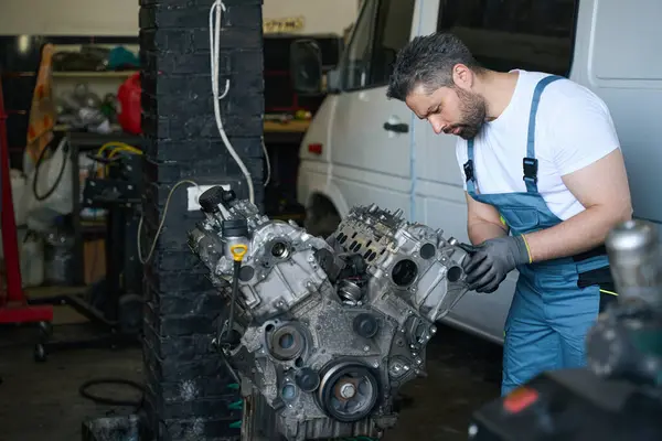 Focused automotive service technician inspecting bolts on cylinder head cover in garage