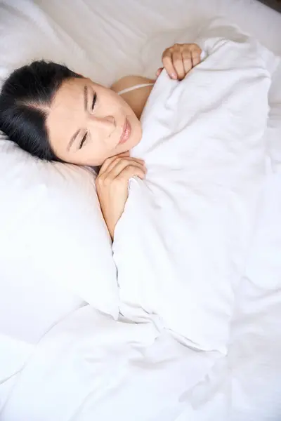 Top view of sleepy adult woman covering herself with blanket while lying in bed on pillow