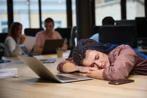 Tired woman with stylish braided hair leaning head on desk and sleeping, overworked lady resting on working place with laptop, exhausted work