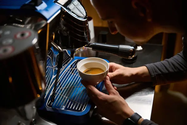 Unrecognizable coffeemaker brewing coffee in espresso machine in coffee shop