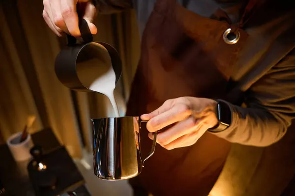 Unrecognizable coffee maker or bartender pouring milk from pitcher preparing coffee in cafe