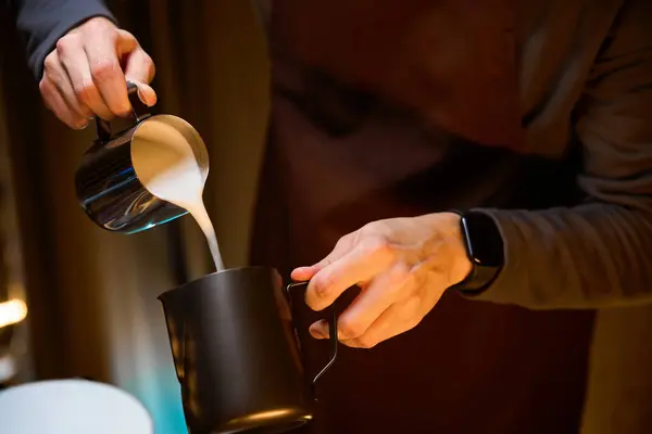 Hands of barista pouring milk from pitcher preparing delicious coffee in coffee house
