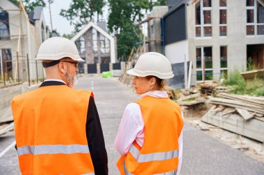 İnşaat müfettişinin yarı inşa edilmiş evlerin arasında yol kenarında dururken müteahhitle konuşması.