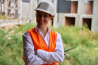 Bitmemiş evlerin arasında duran gülümseyen inşaat şefinin belden yukarı portresi.