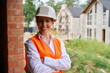 Yarı inşa edilmiş konutların arasında duran neşeli bina müfettişinin belden yukarı portresi.