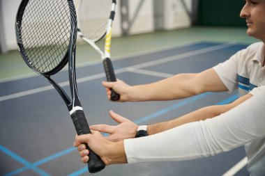 Gülen adam eğitmeni ve kadın tenis antrenmanı. İç sahada tekniği geliştiriyor.