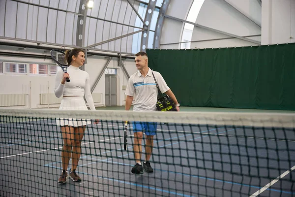 Fit woman with man instructor after playing tennis game at indoor court