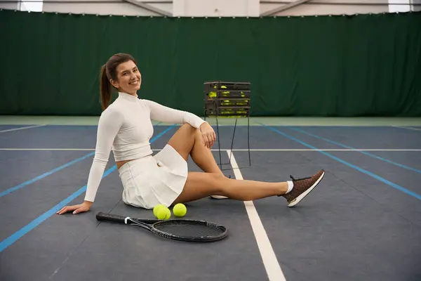 Sporty woman with tennis racket sitting on tennis court after enjoyable game