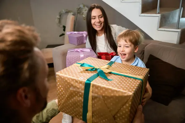 Bir adam Noel tatilini evinde ailesiyle birlikte kutlarken küçük oğluna hediye veriyor.